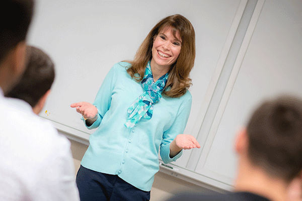 Emily Cannon, DNP, Associate Professor of Nursing, teaches a group of nursing students in one of the newly renovated classrooms for nursing students at Indiana State University. The smiling woman with brown hair is standing at the front of the classroom and is wearing a light blue blouse and dark slacks.